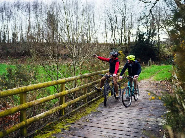2 personnes en train de faire du vélo sur un pont en bois dans la campagne normande