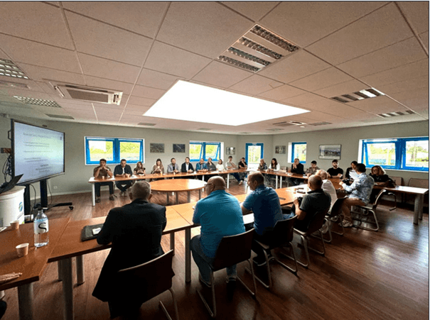 Personnes autour d'une table de réunion en U et regardant une présentation sur un écran